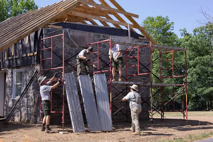 A four-person crew putting up scaffolding against a stone house with new roof rafters
