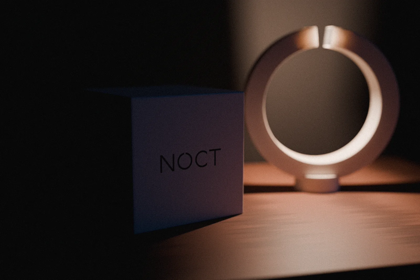 A bone-coloured box beside the glowing NOCT lamp, the NOCT wordmark printed on its face.